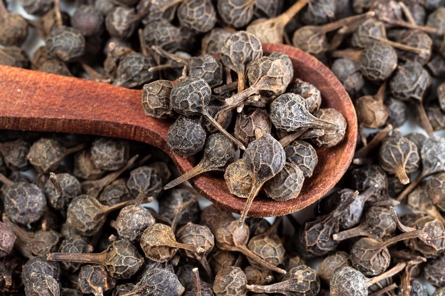 Whole cubeb peppercorns with visible tails in and around a wooden spoon